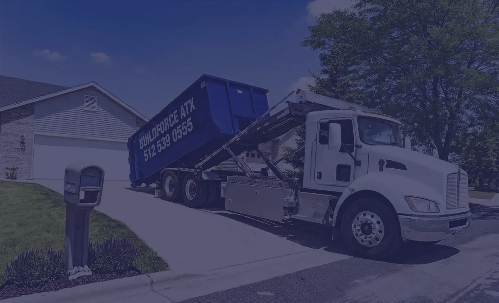 Dumpster Delivery in Austin TX | BuildForce ATX Roll-Off Services BuildForce ATX dumpster delivery truck placing a blue roll-off dumpster in a residential driveway in Austin, Texas.