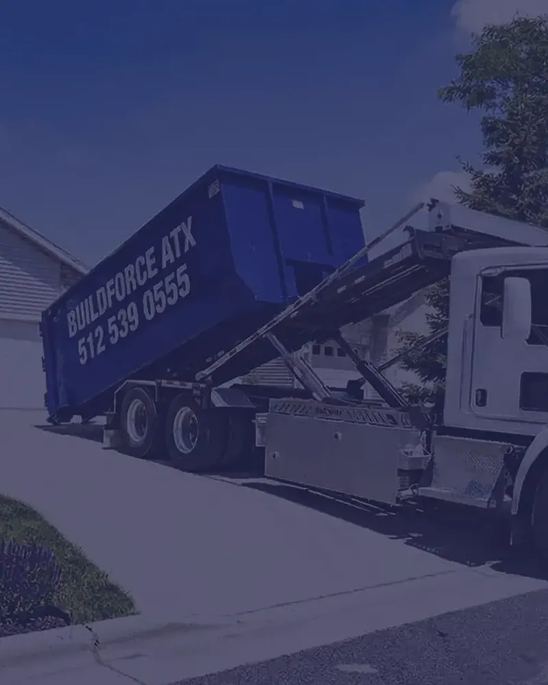 Dumpster Delivery in Austin TX | BuildForce ATX Roll-Off Services BuildForce ATX dumpster delivery truck placing a blue roll-off dumpster in a residential driveway in Austin, Texas.